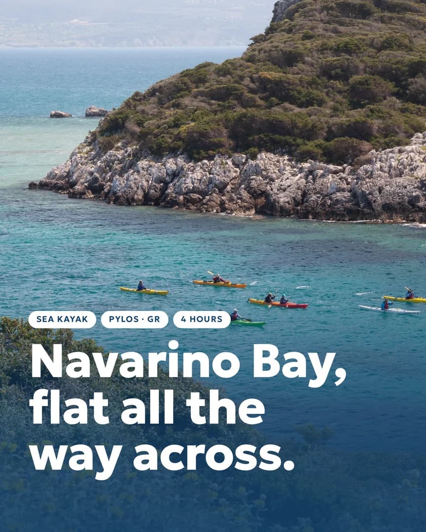 Sea kayakers crossing the flat turquoise water of Navarino Bay below a rocky green headland.