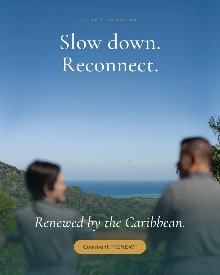 Two guests in grey robes look out from a mountain rail at Isla over green hills to the Caribbean.