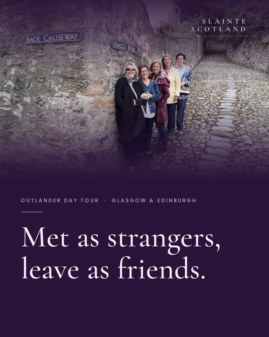 Five smiling Slàinte Scotland guests together by an old stone wall on a cobbled Scottish lane.